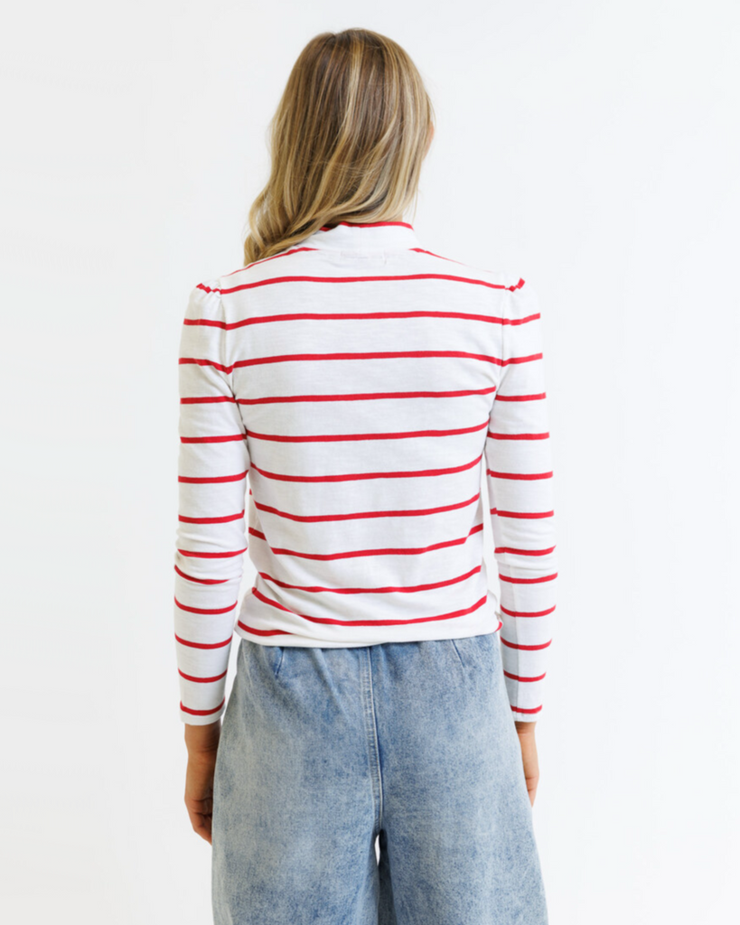 Woman wearing a white long-sleeve shirt with red stripes and blue jeans on a white background