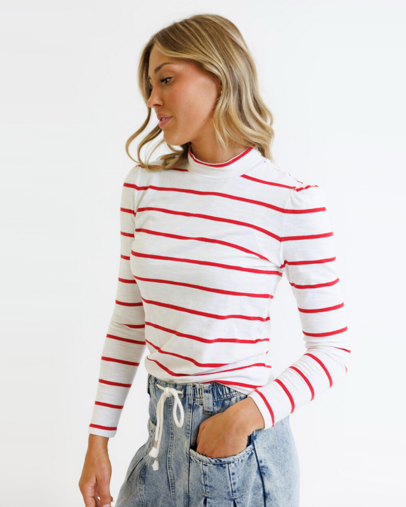 Woman wearing a white long-sleeve shirt with red stripes and blue jeans on a white background