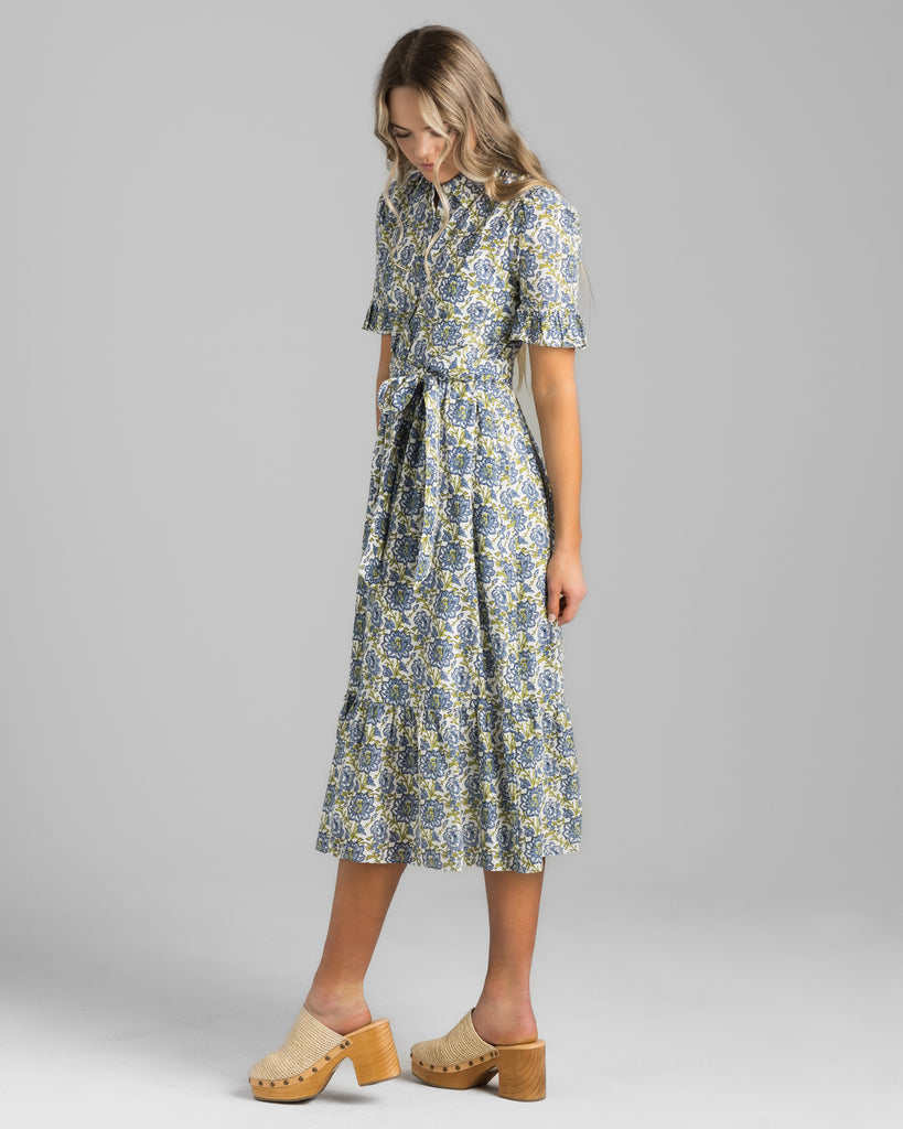 Model wearing a blue and green floral print, short sleeve with ruffles, buttondown, collared, midi length dress.