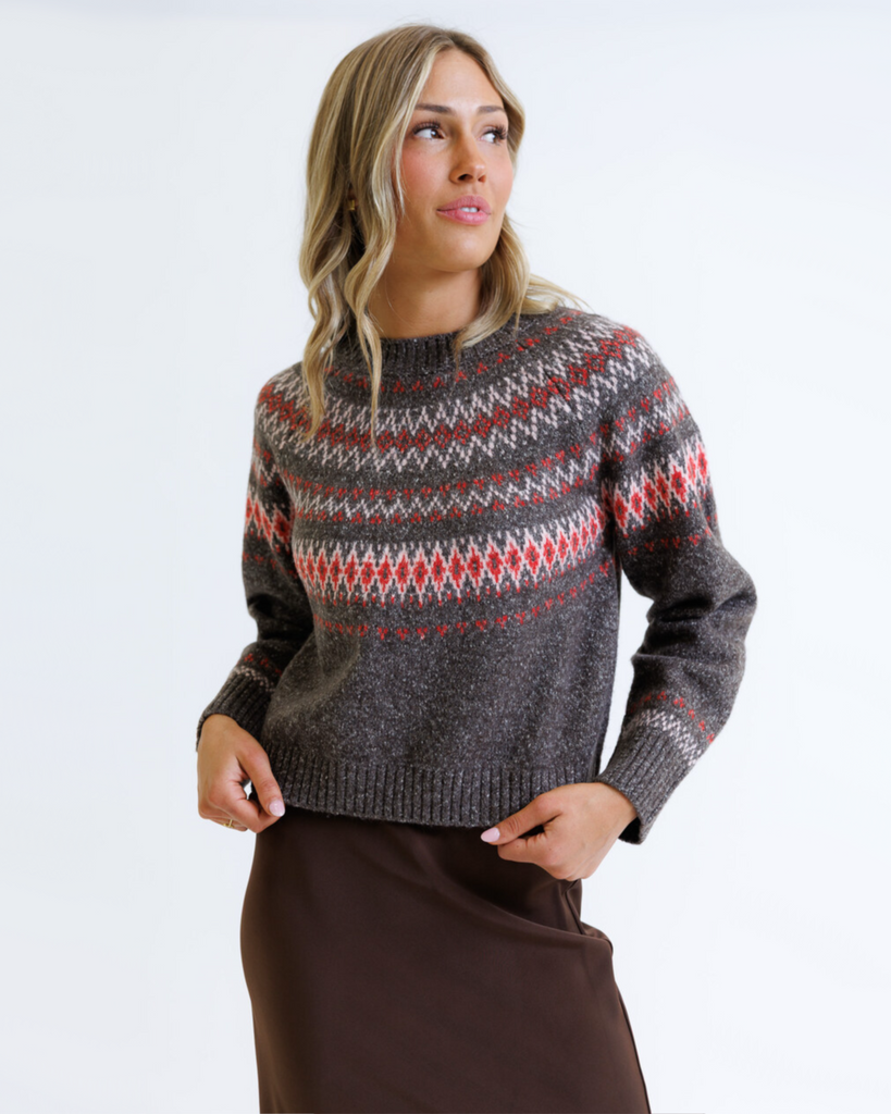Woman wearing a multicolored geometric printed sweater with brown skirt on a white background