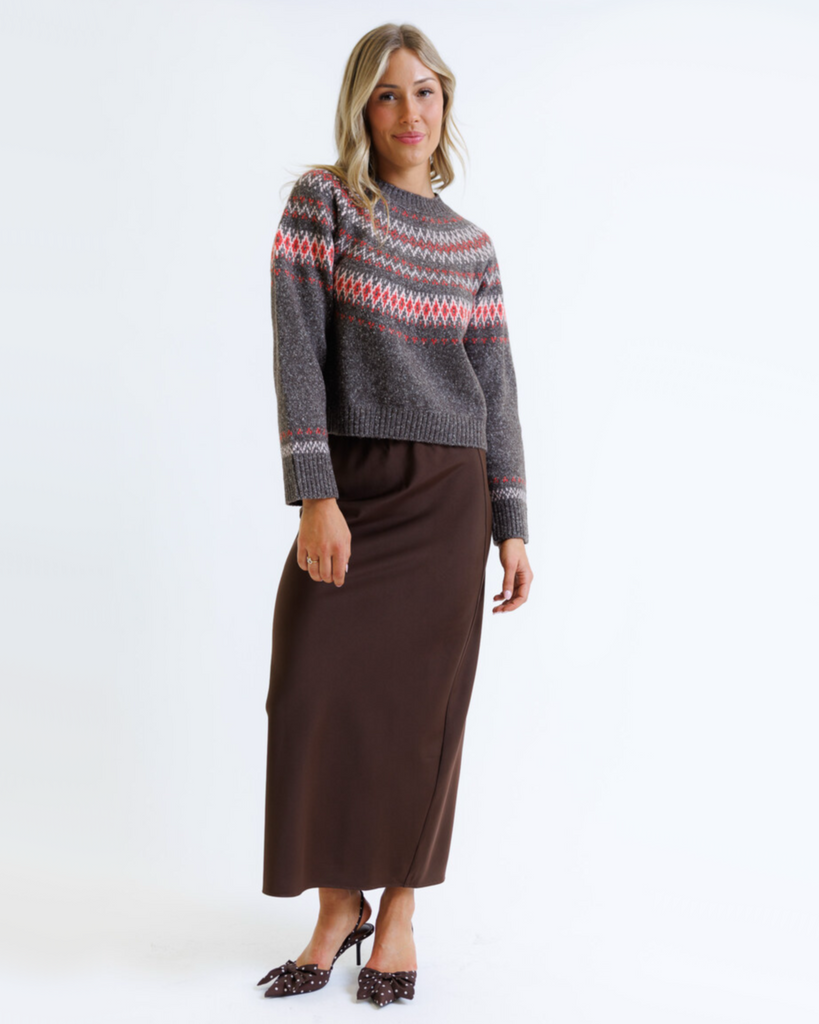Woman wearing a multicolored geometric printed sweater with brown skirt on a white background