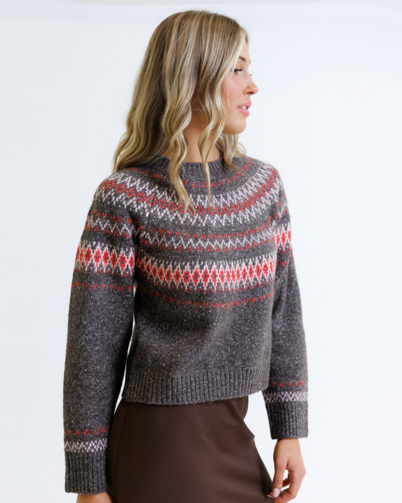 Woman wearing a multicolored geometric printed sweater with brown skirt on a white background