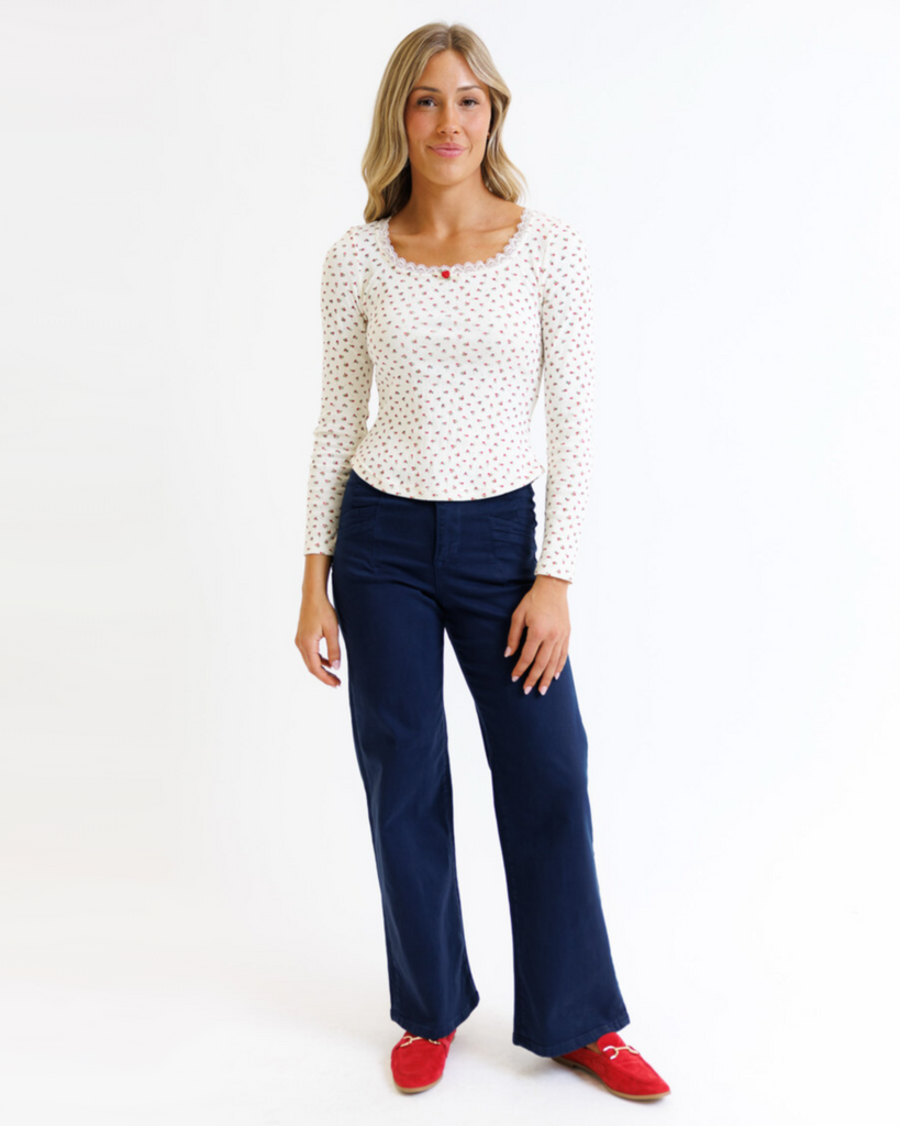 Woman wearing cream floral long sleeve with pointelle fabric and dark jeans on a white background