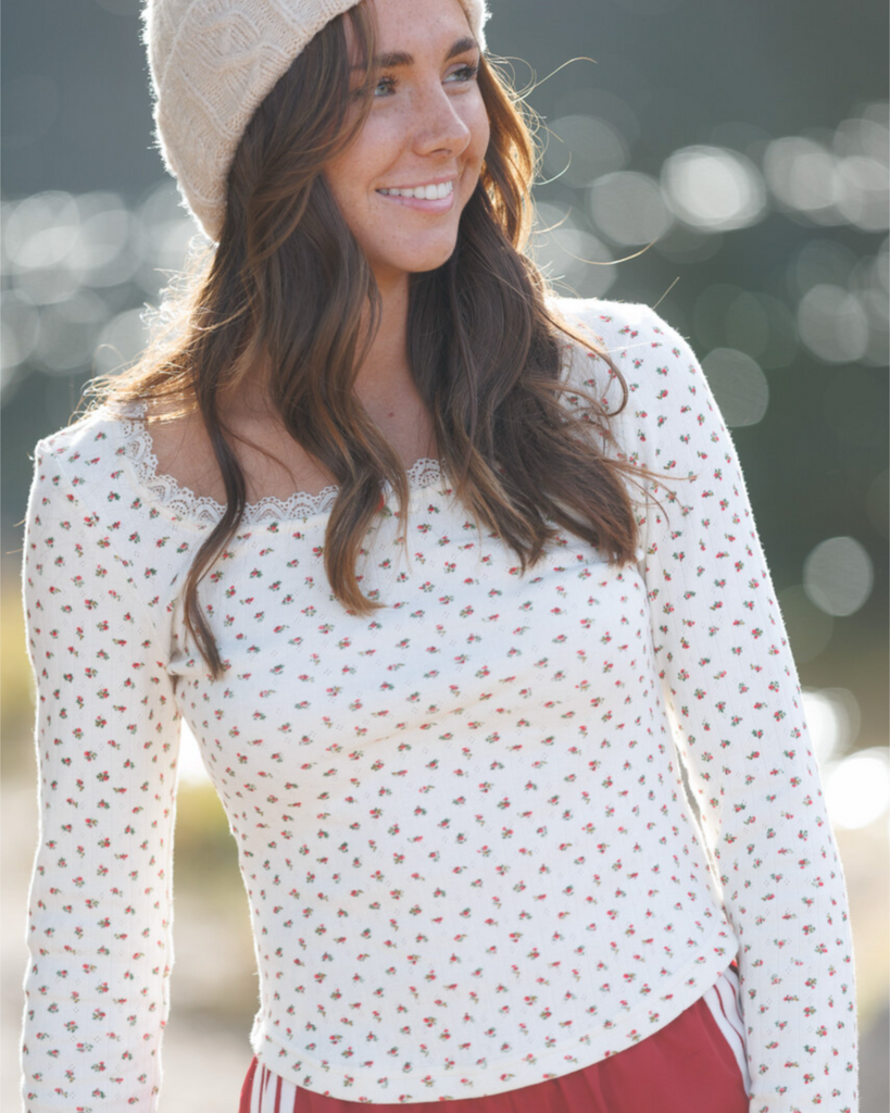 Woman wearing a white floral blouse and beige beanie with a blurred natural background