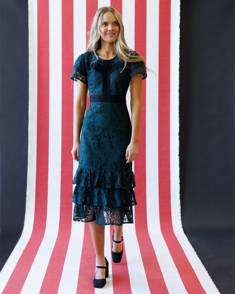 Woman wearing a dark green lace dress standing against a red, white, and black striped background