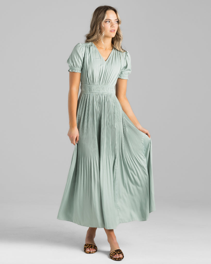 Model wearing a green short sleeve, v-neck maxi dress with pleating down the skirt.