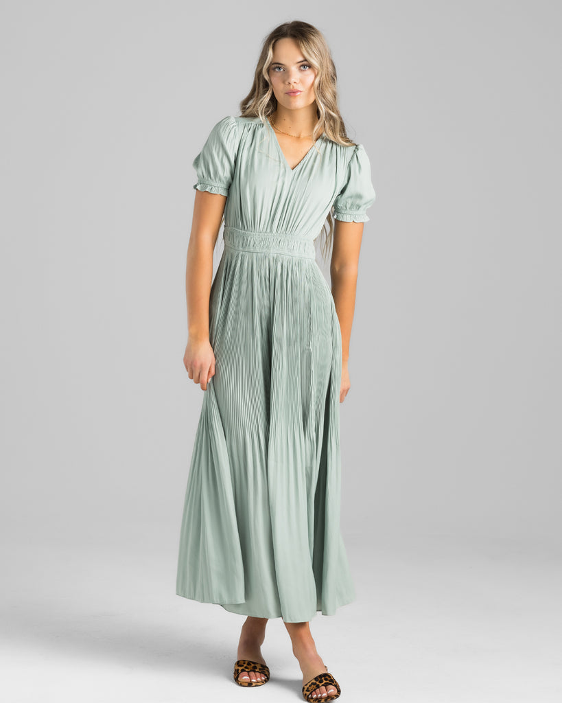 Model wearing a green short sleeve, v-neck maxi dress with pleating down the skirt.