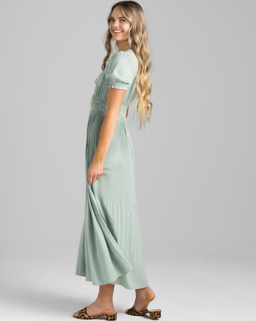 Model wearing a green short sleeve, v-neck maxi dress with pleating down the skirt.