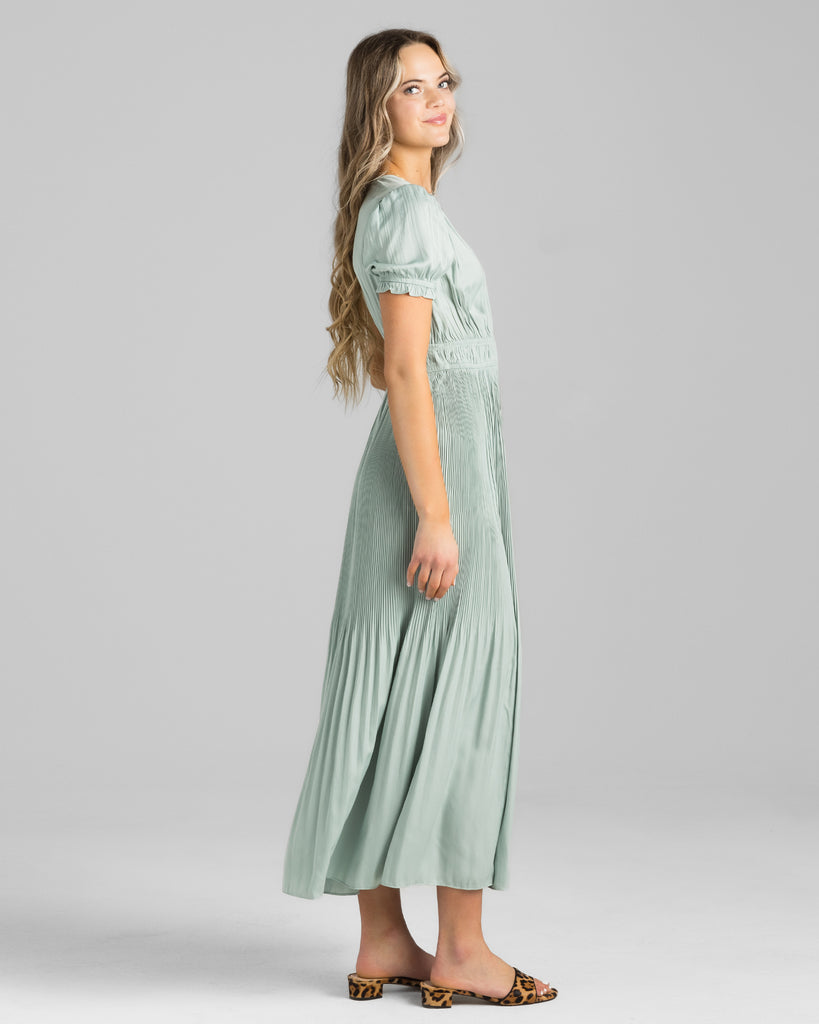 Model wearing a green short sleeve, v-neck maxi dress with pleating down the skirt.