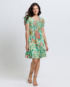 Model wearing a green with pink and yellow floral print short sleeve square neck knee length dress.