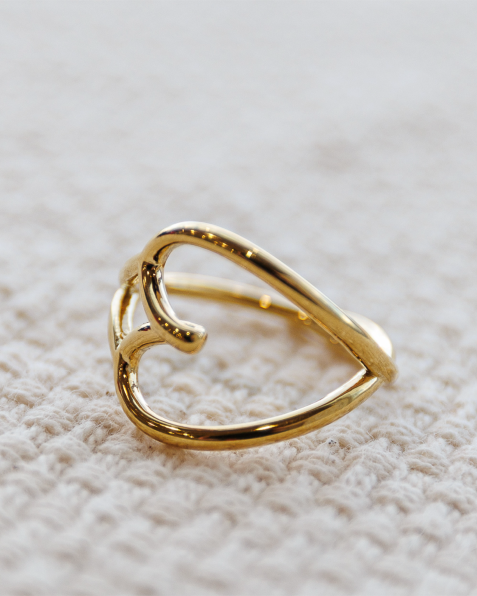 Gold heart-shaped ring on a textured beige surface
