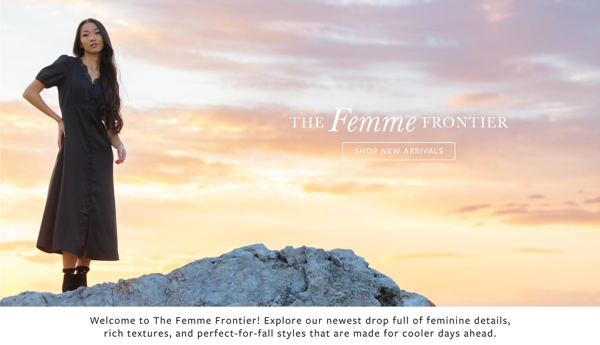 A woman wearing a dark charcoal gray midi dress stands on a rocky outcrop against a warm sunset sky. Large text reads 'THE Femme FRONTIER' with a 'SHOP NEW ARRIVALS' button, and a welcome banner appears along the bottom.
