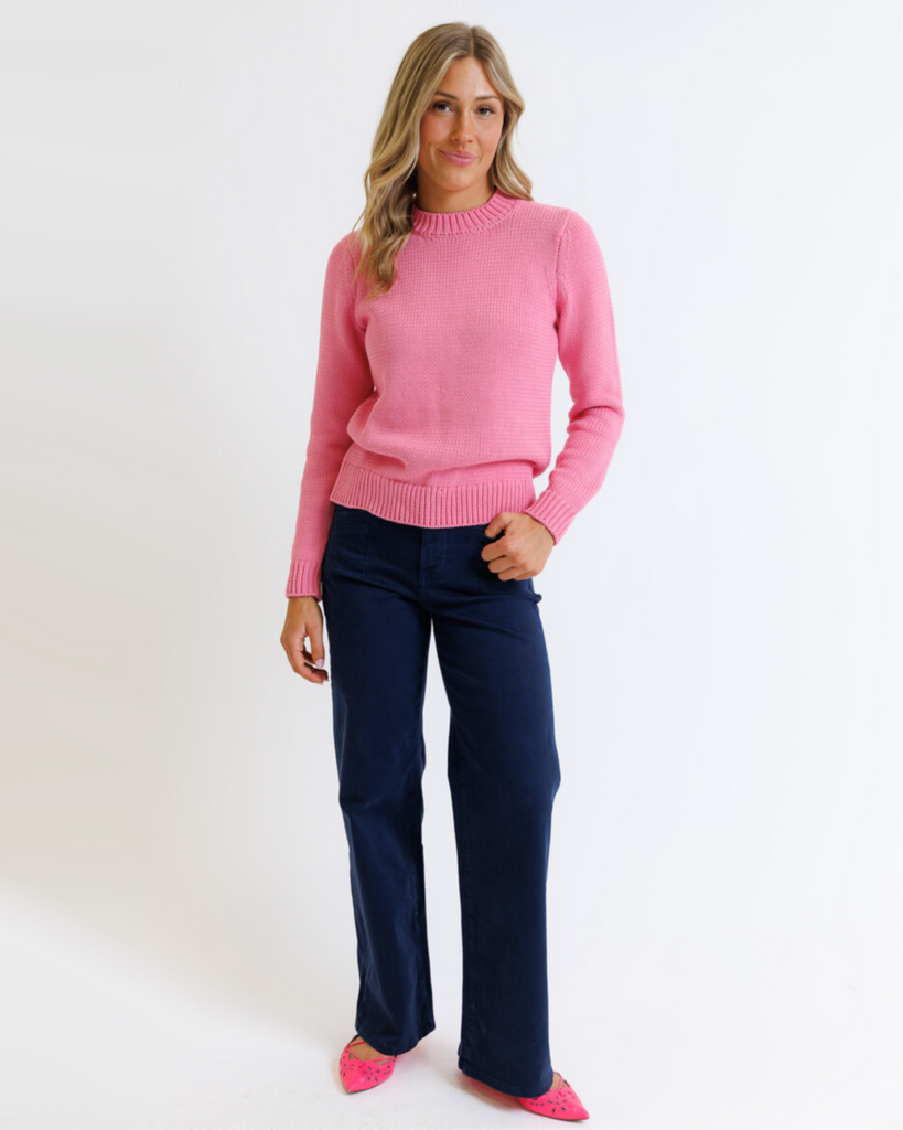 Woman wearing a pink sweater and navy pants on a white background