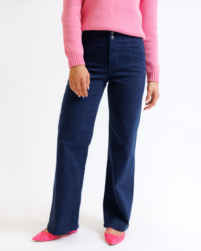 Woman wearing a pink sweater and navy pants on a white background