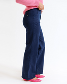 Woman wearing a pink sweater and navy pants on a white background