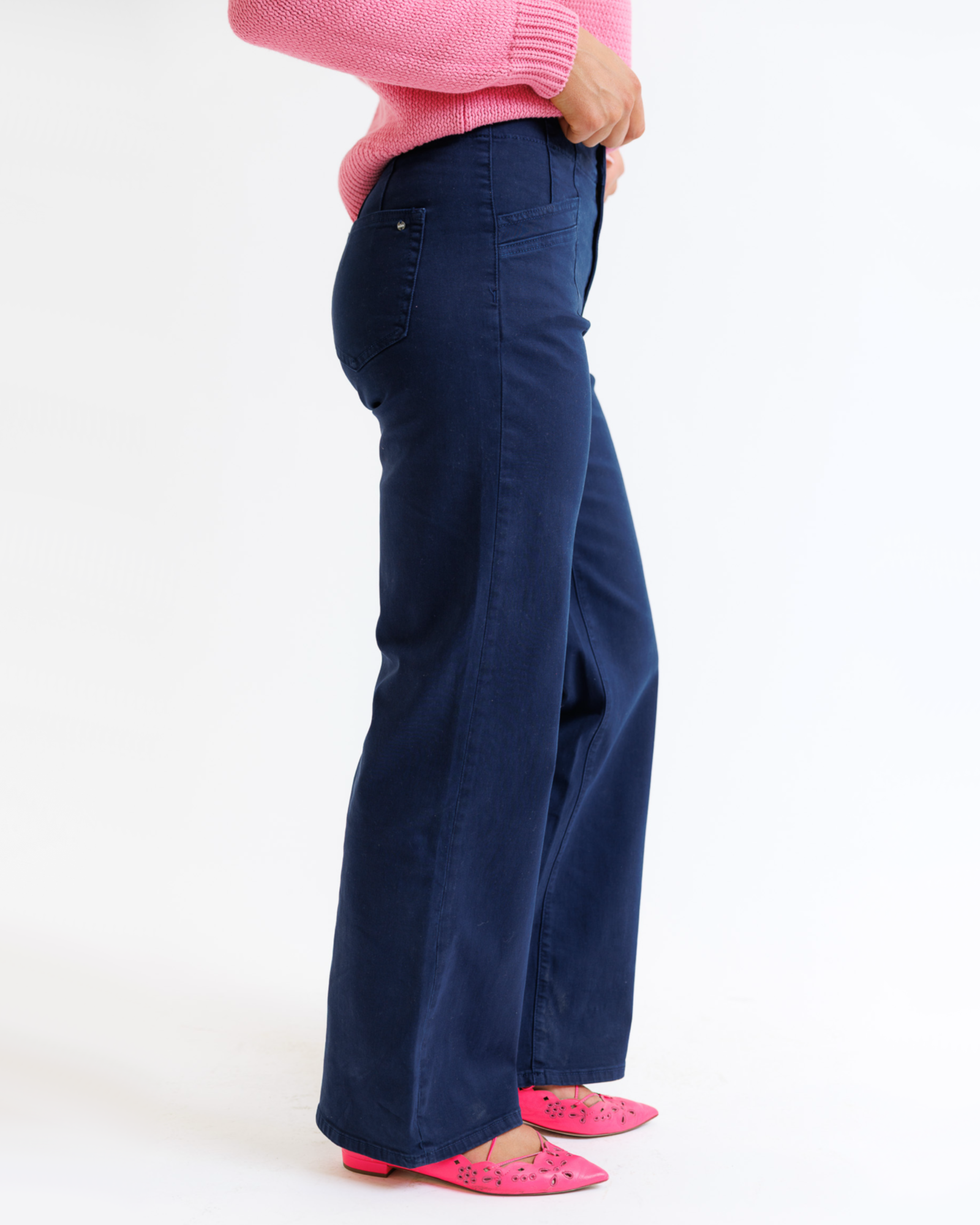 Woman wearing a pink sweater and navy pants on a white background