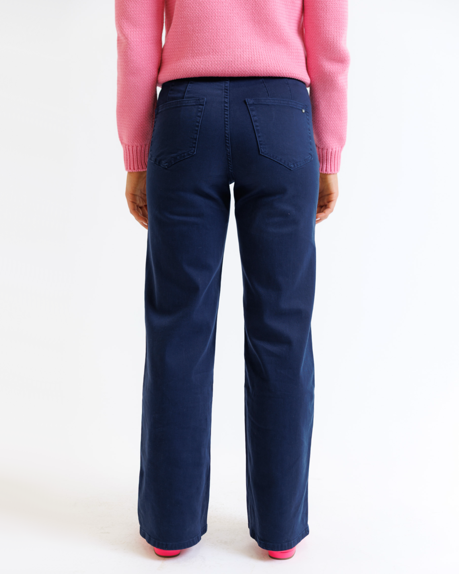 Woman wearing a pink sweater and navy pants on a white background