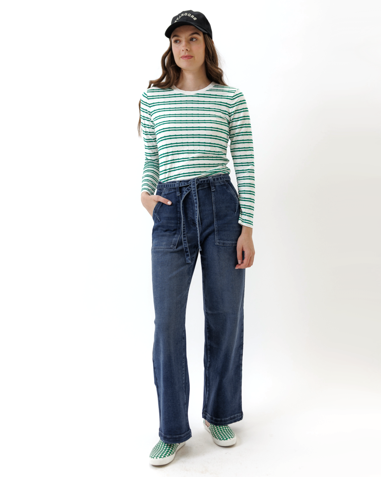 Woman wearing a green and white striped shirt and blue jeans on a white background