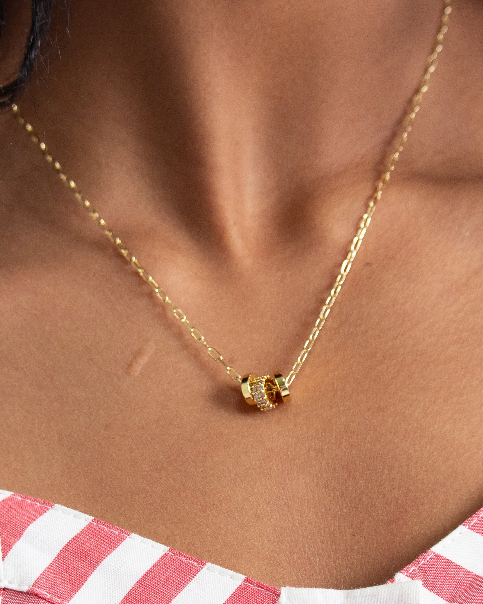 Gold necklace with a pendant on a person wearing a striped shirt.