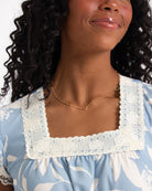 Woman wearing a blue floral dress with a white lace collar against a white background
