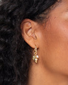 Close-up of an ear wearing a gold earring with leaf-like charms.