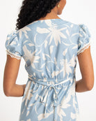 Woman wearing a blue floral dress with lace trim on a white background