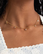 Gold necklace with star pendants on a person wearing a white top.