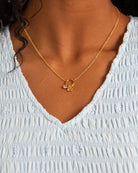 Gold necklace with a pendant worn by a person in a light blue top.
