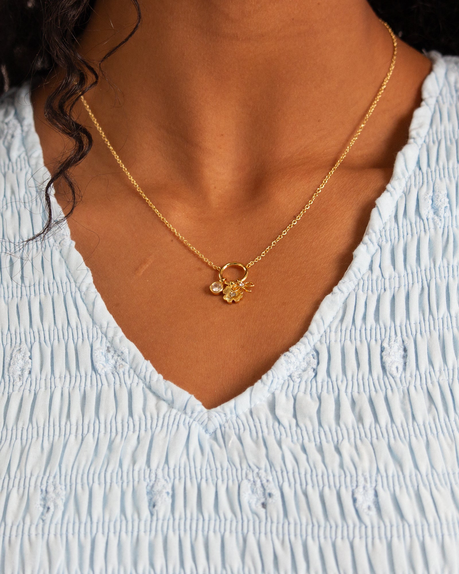 Gold necklace with a pendant worn by a person in a light blue top.