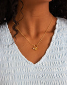 Gold necklace with a pendant worn by a person in a light blue top.