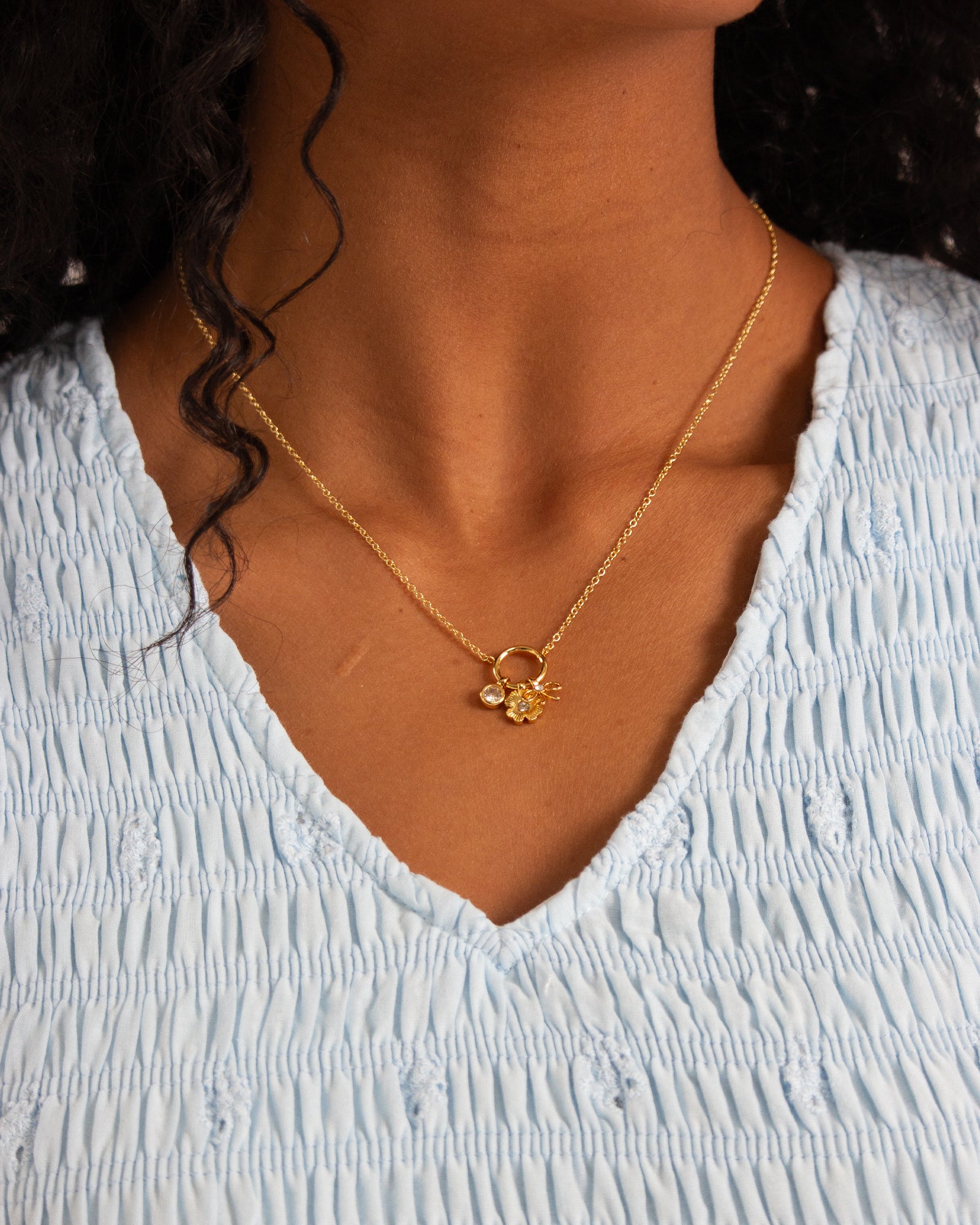 Gold necklace with a pendant worn by a person in a light blue top.