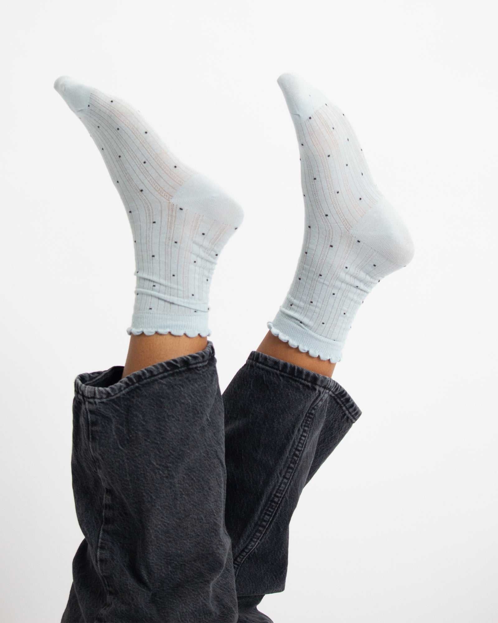 White socks with black polka dots worn with dark jeans on a white background