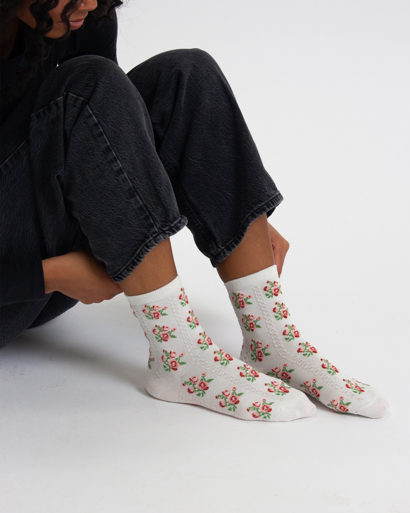 Person wearing white socks with floral pattern sitting on a light gray background