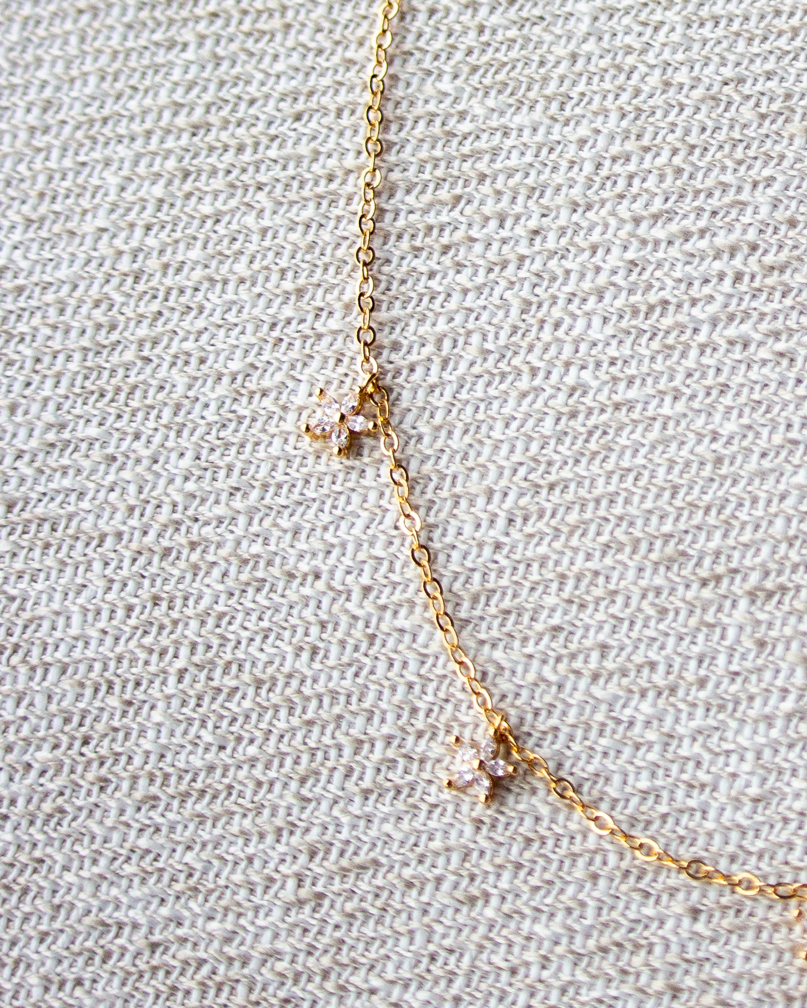 Delicate gold necklace with small pendants on a textured beige fabric background