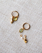 Gold earrings with gemstones on a textured beige fabric background