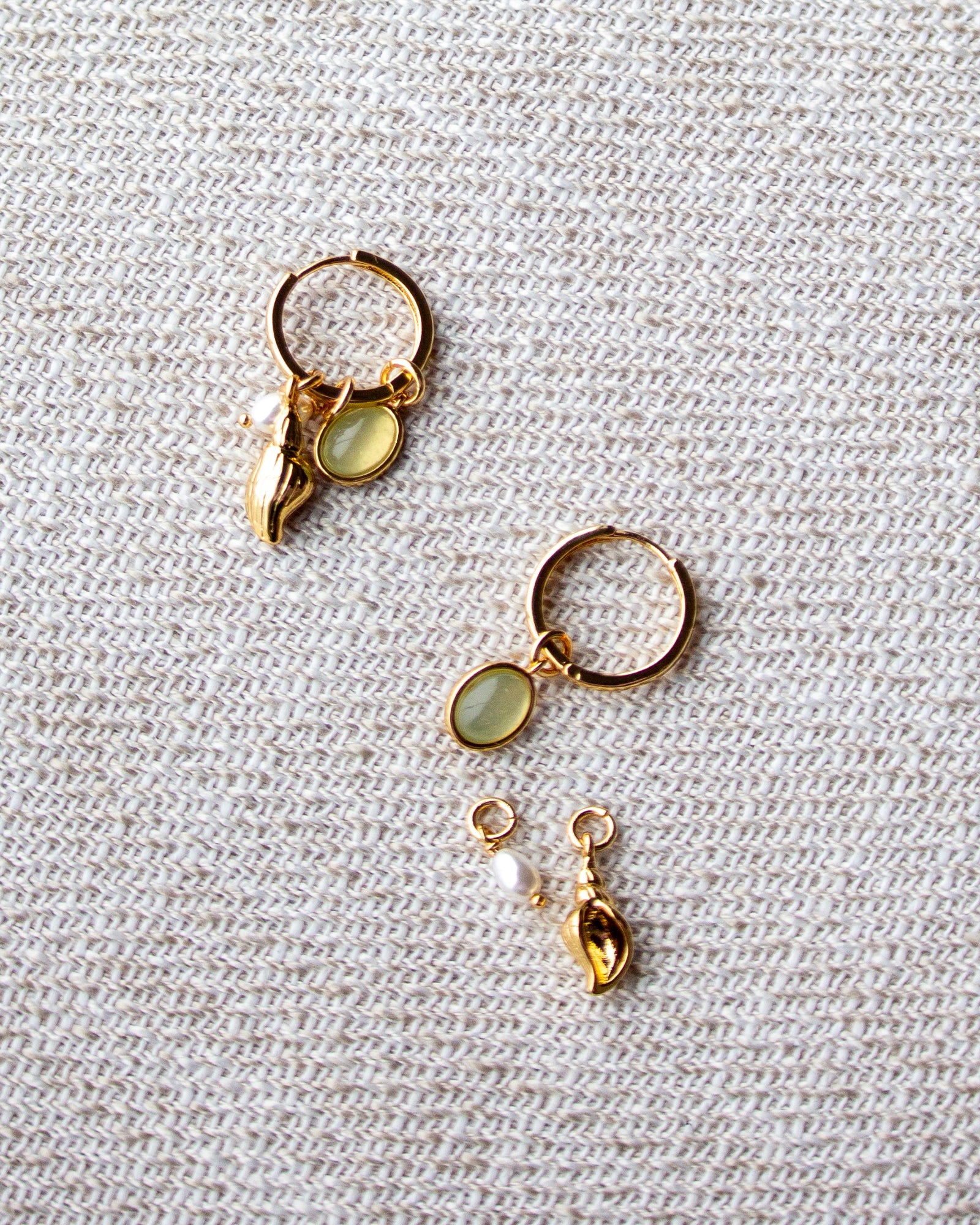 Gold earrings with gemstones on a textured beige fabric background