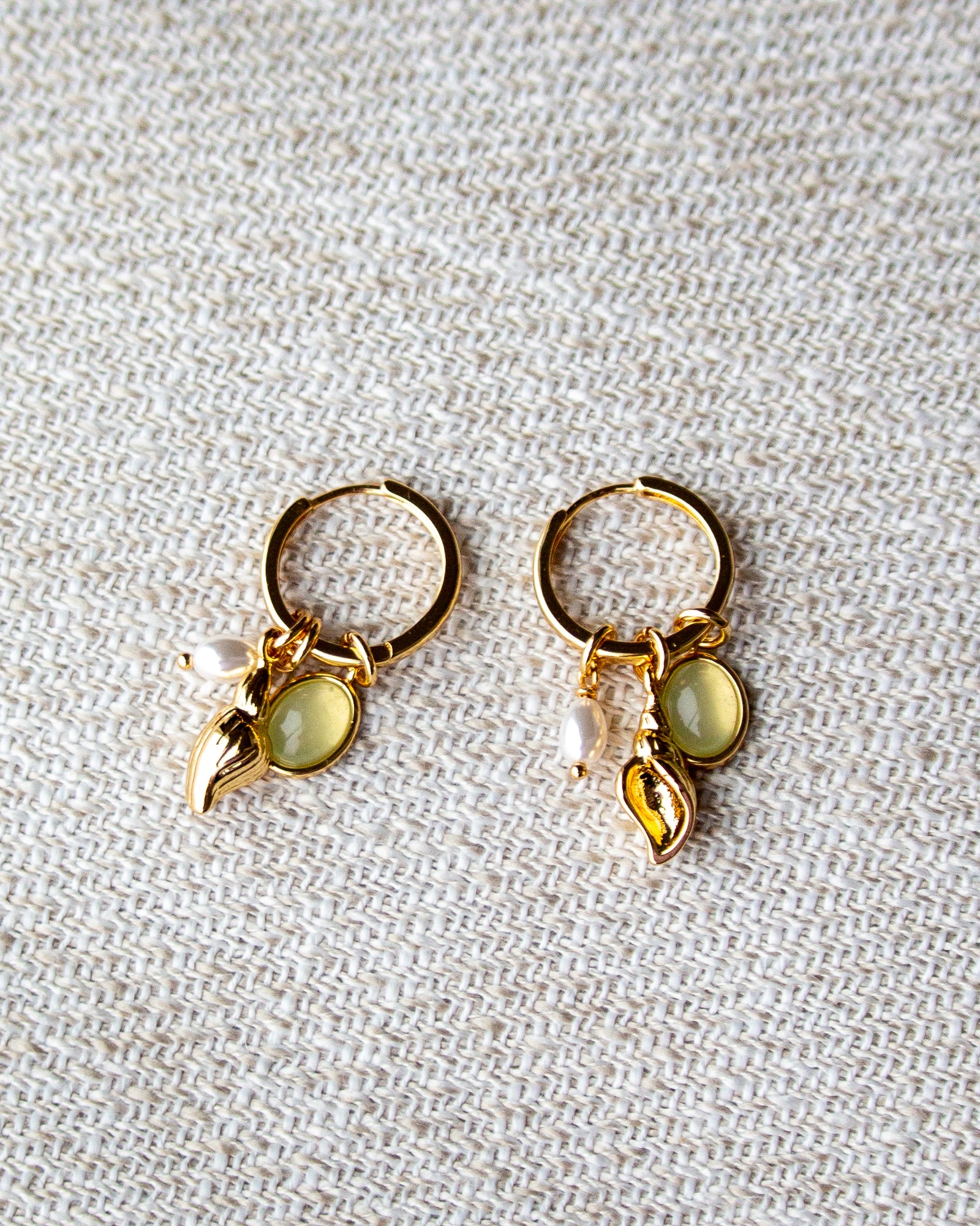 Pair of gold hoop earrings with green gemstones on a textured beige background