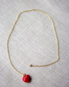 Gold necklace with a red heart pendant on a light gray background