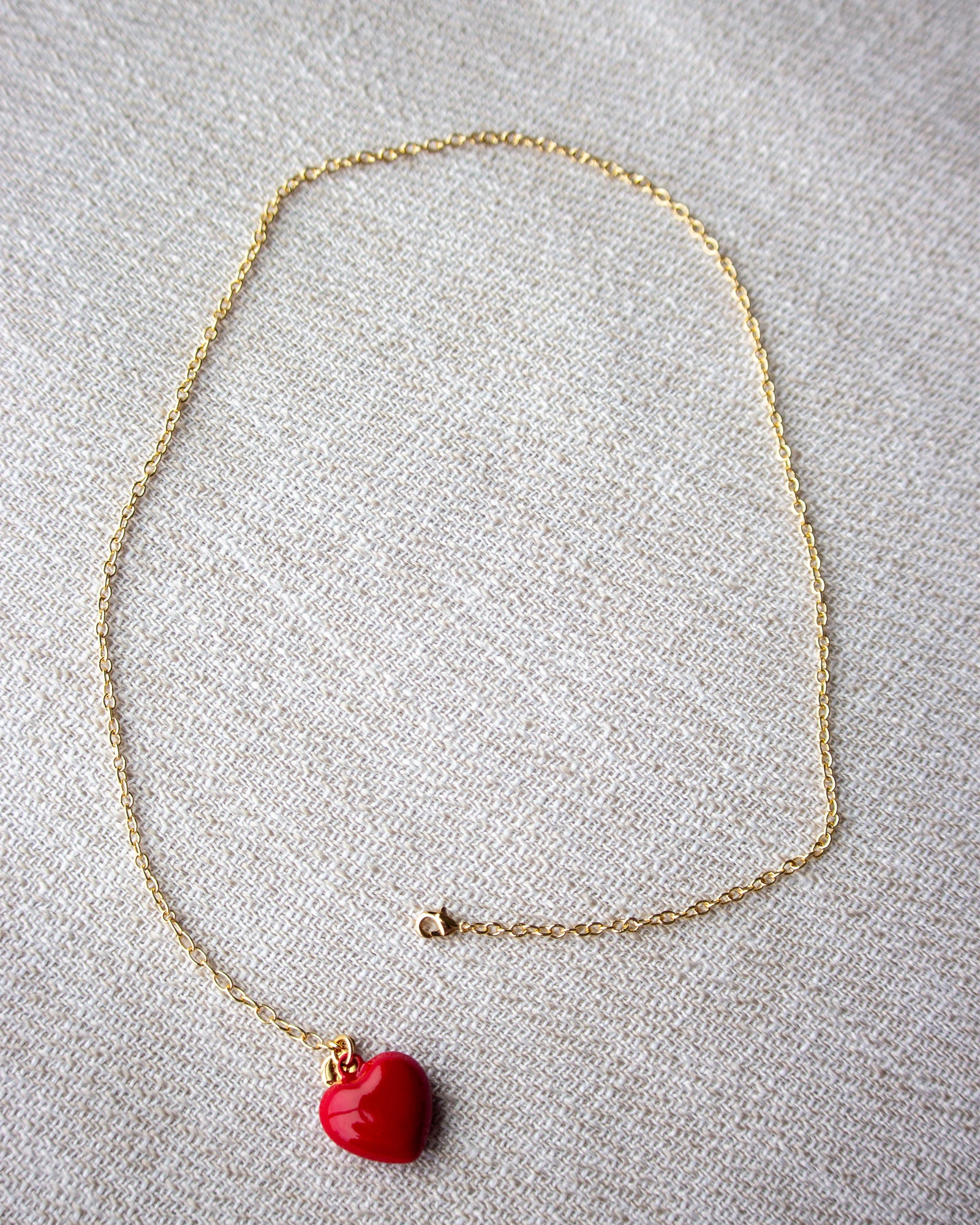 Gold necklace with a red heart pendant on a light gray background
