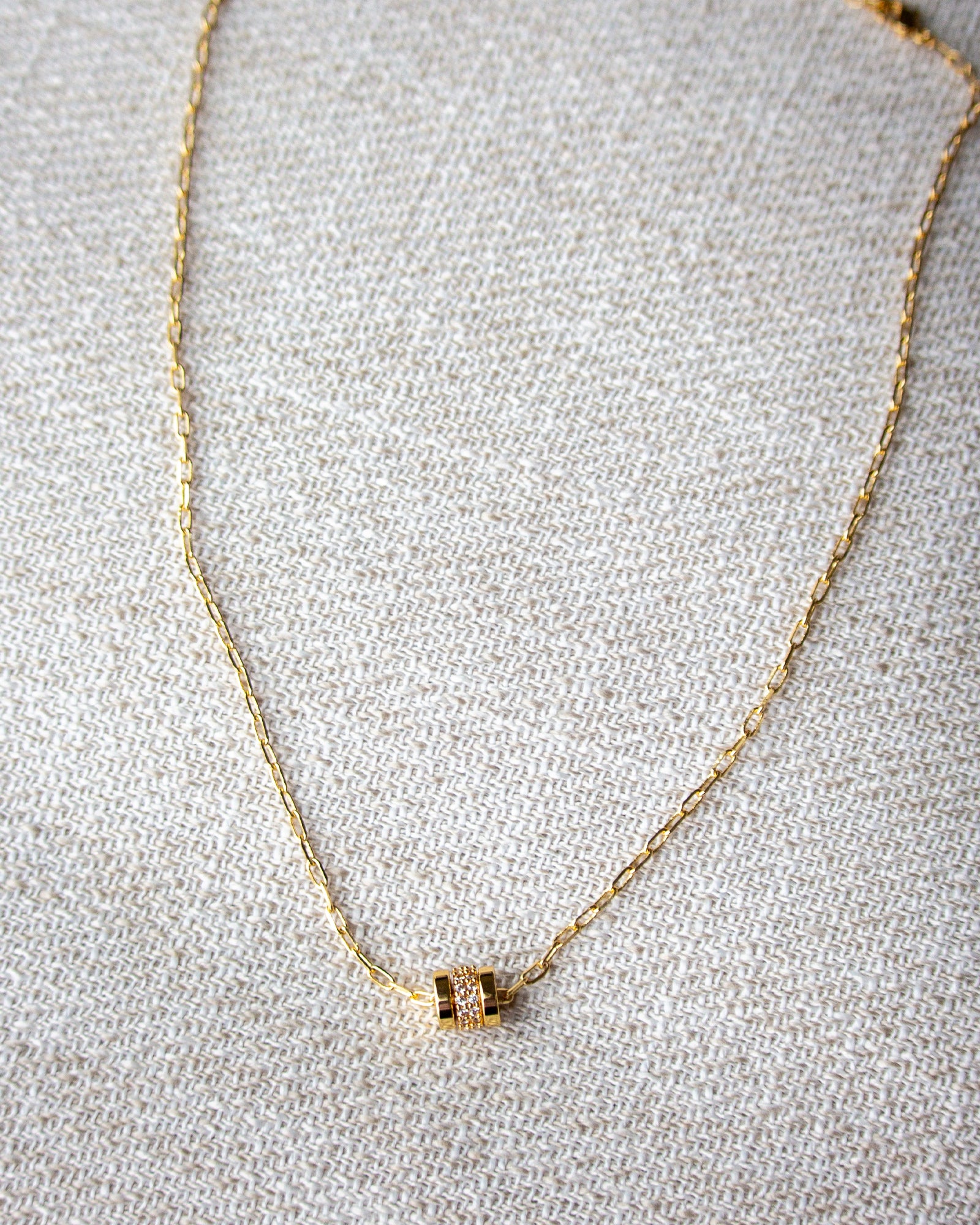 Gold necklace with a small pendant on a textured gray surface