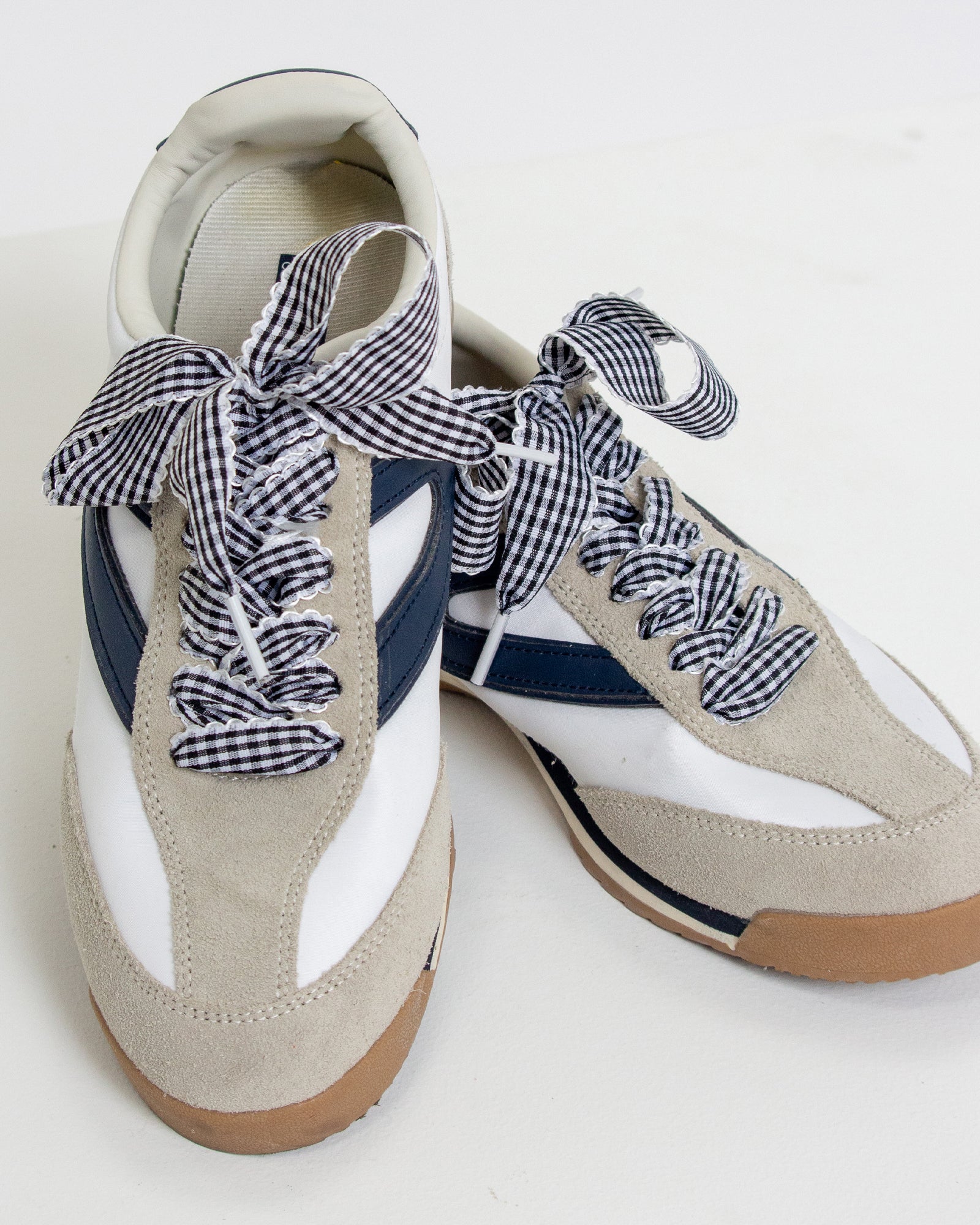 Beige sneakers with navy and white checkered laces on a white background