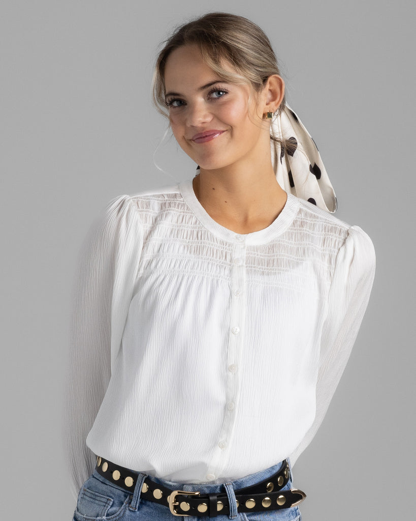 Model wearing a white long sleeve sheer blouse with smocking on yoke.