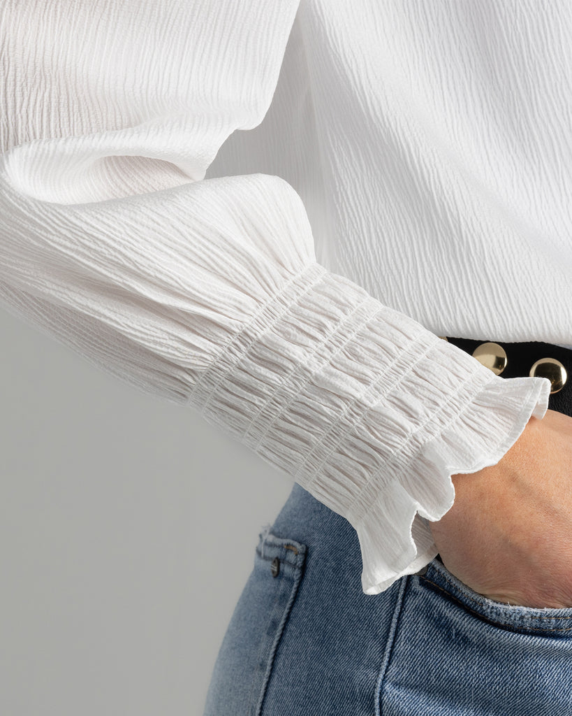 Up close image of model wearing a white blouse with smocking on sleeve cuff.