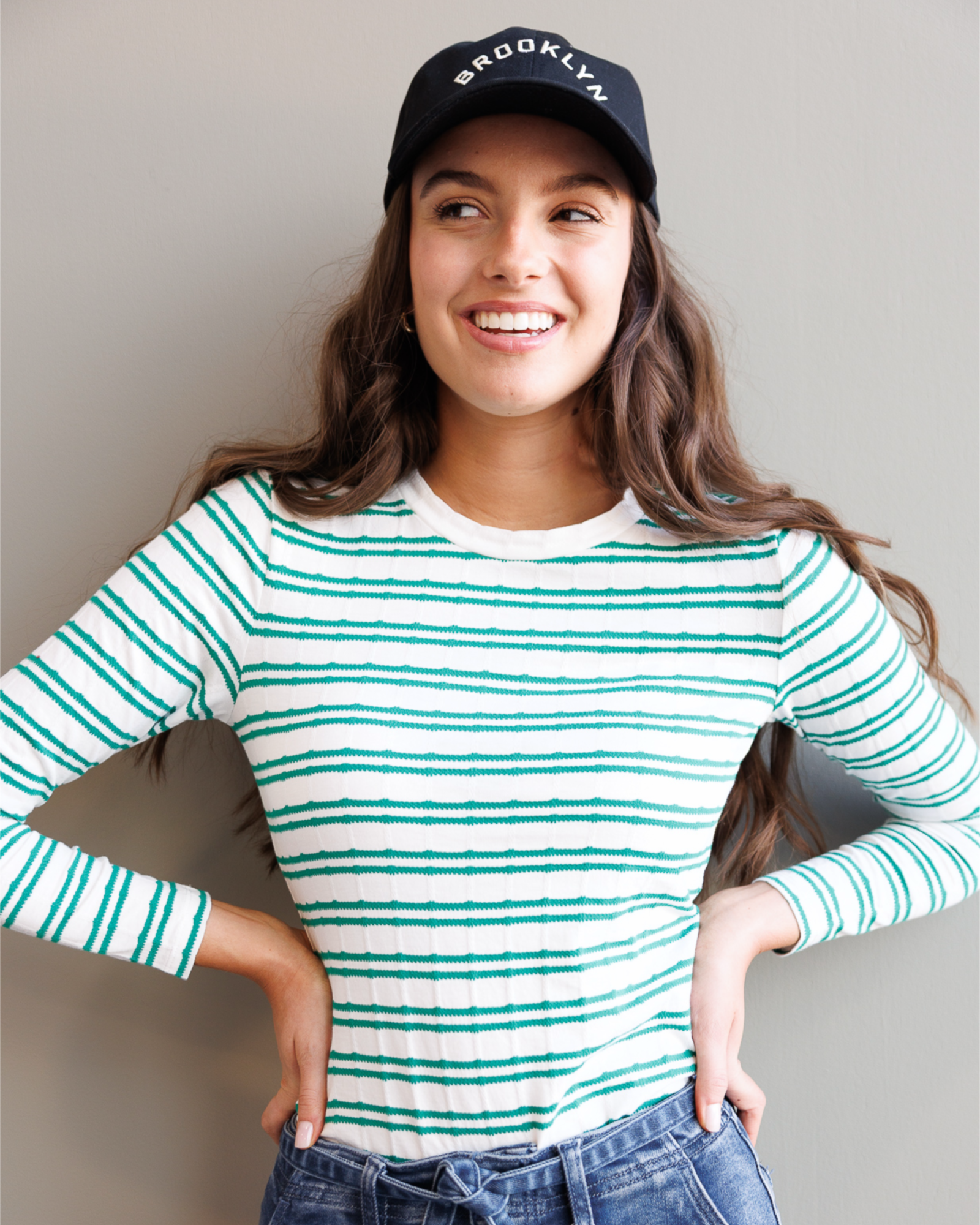 Woman wearing a striped shirt and cap with 'Brooklyn' text on a plain background