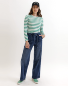 Woman wearing a green and white striped shirt, blue jeans, and a black cap on a white background