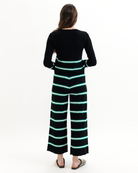 Woman wearing a black sweater and striped pants with green accents on a white background