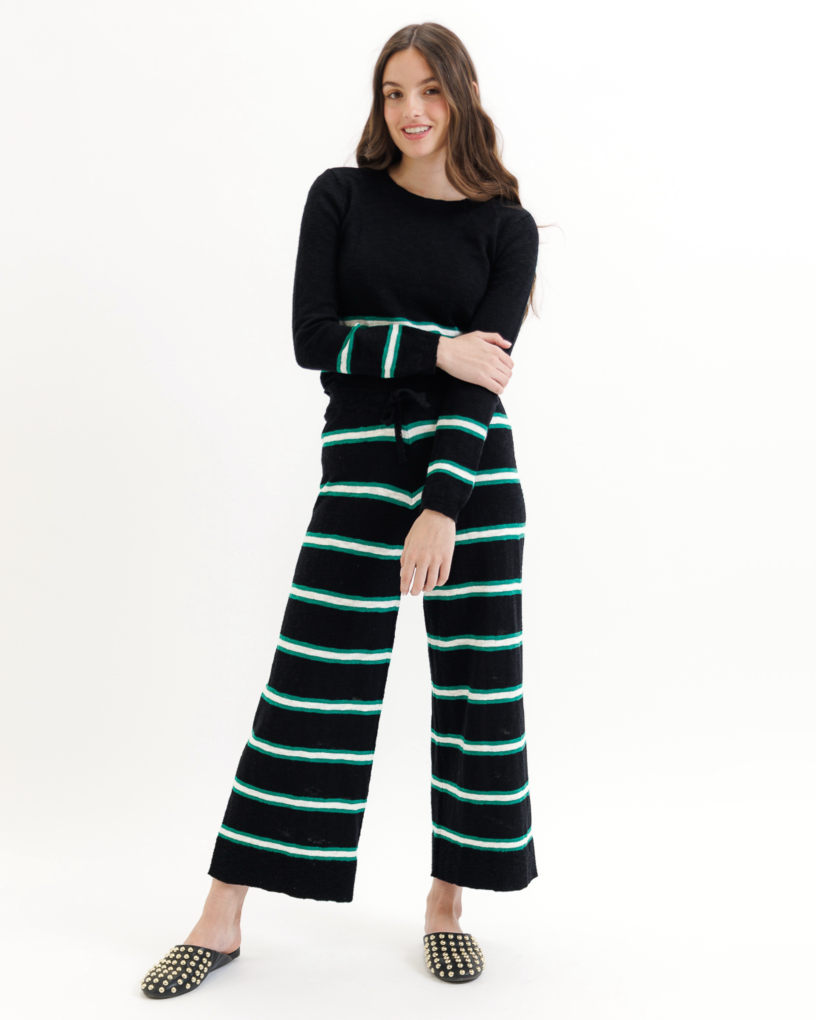 Woman wearing a black sweater and striped pants with green accents on a white background