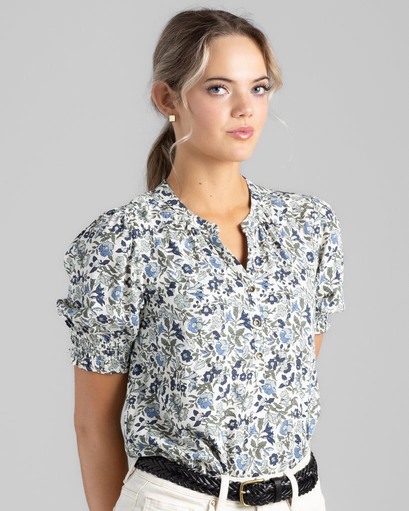 Model wearing a blue floral print short sleeve blouse with a mandarin collar.