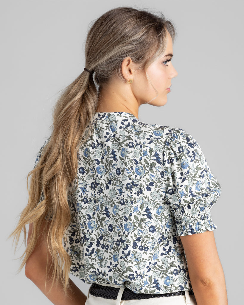 Model wearing a blue floral print short sleeve blouse with a mandarin collar.