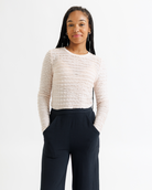Woman wearing a cream lace top and dark wide-leg pants on a white background